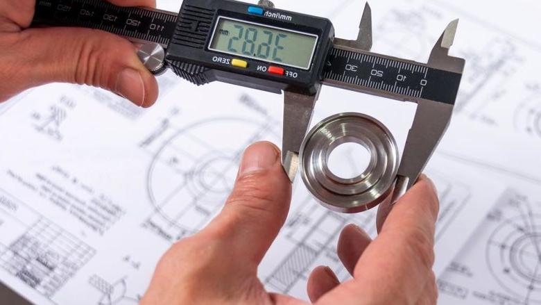 质量工程师用卡尺测量生产零件以确保其符合要求, 在后台有一个参考图.